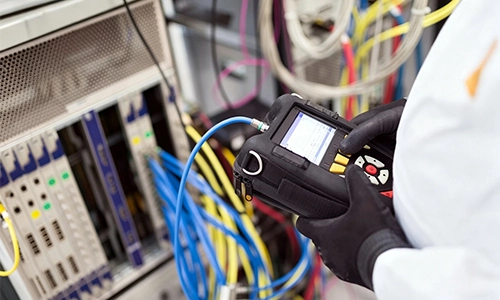 Technician using a handheld testing device to inspect and verify hardware equipment system wiring.