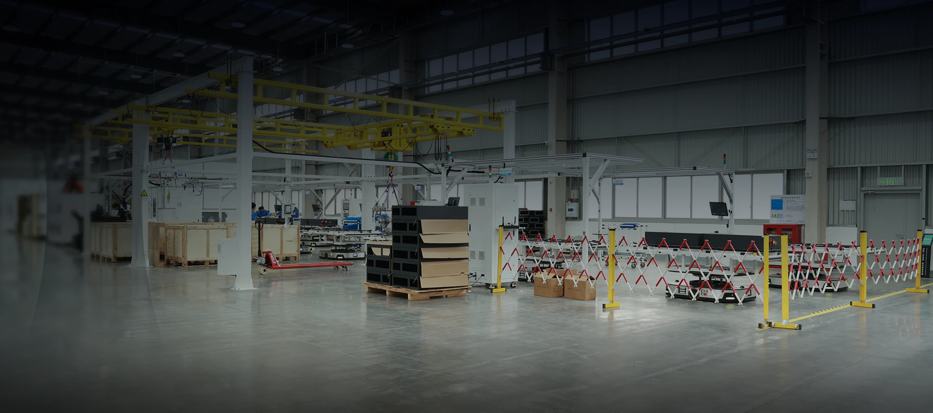 Spacious factory floor showcasing automated assembly lines, overhead gantry cranes, and staged battery enclosure components.