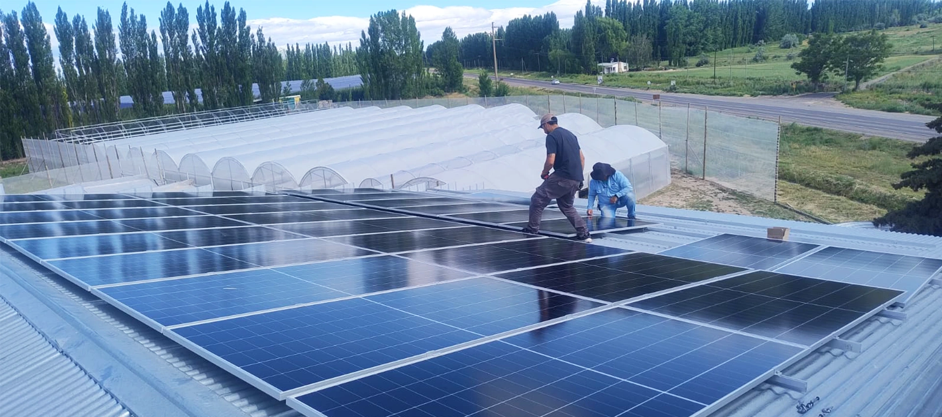 Technicians installing rooftop solar panels on a commercial facility near greenhouses in Argentina.