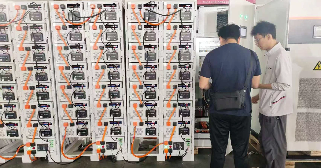 Two engineers reviewing parameters and conducting system checks in front of battery storage racks and a control cabinet.