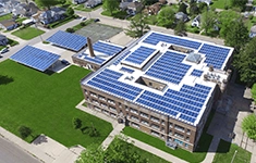 Aerial view of a commercial building and solar carports fitted with rooftop solar panels in a suburban setting.