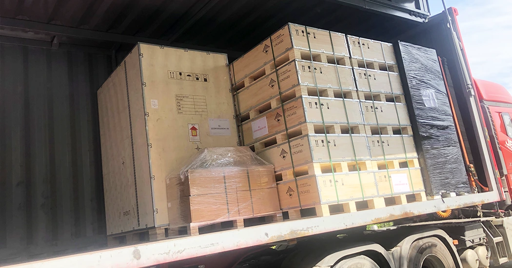 Wooden crates with hazard labels and packaged energy equipment securely loaded inside a shipping container on a truck.