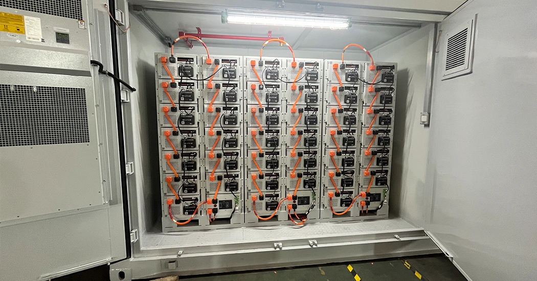 Interior view of an open energy storage container showing vertical racks of battery modules with orange high-voltage cables.