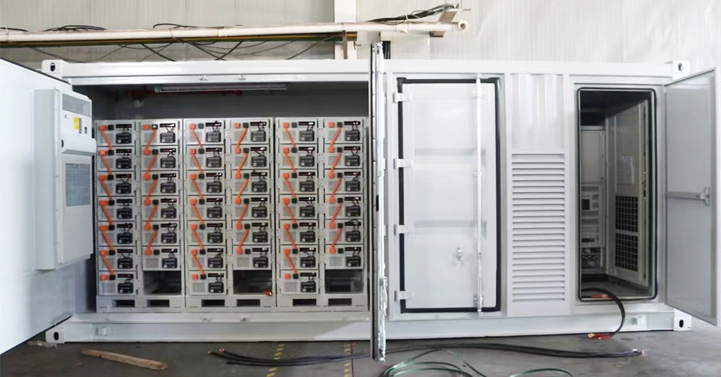 Side view of an open white energy storage container showing battery racks with orange cabling and control compartments.