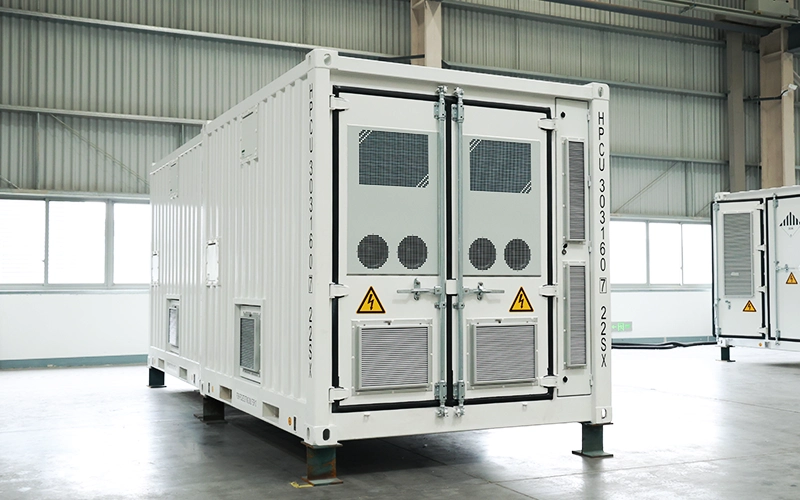 Rear view of a white energy storage container showing heavy-duty closed doors, ventilation fans, air filter grilles, and high-voltage warning labels inside a warehouse.