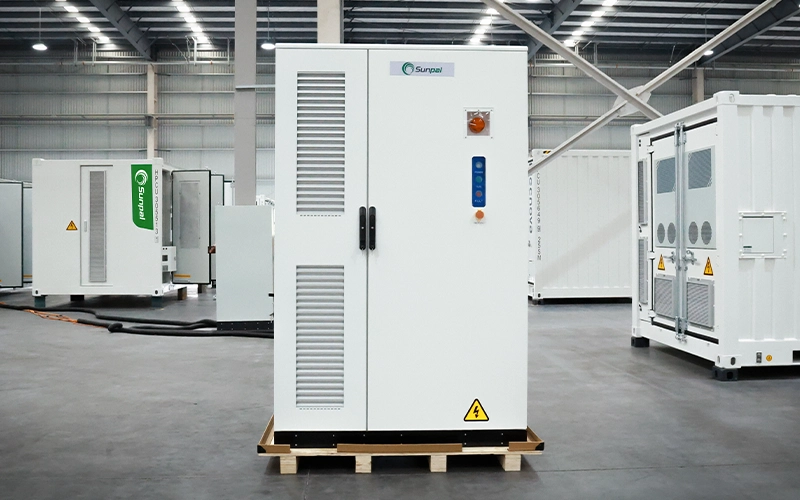 Front view of a white Sunpal commercial energy storage cabinet mounted on a wooden pallet inside a manufacturing facility, with larger storage containers visible in the background.