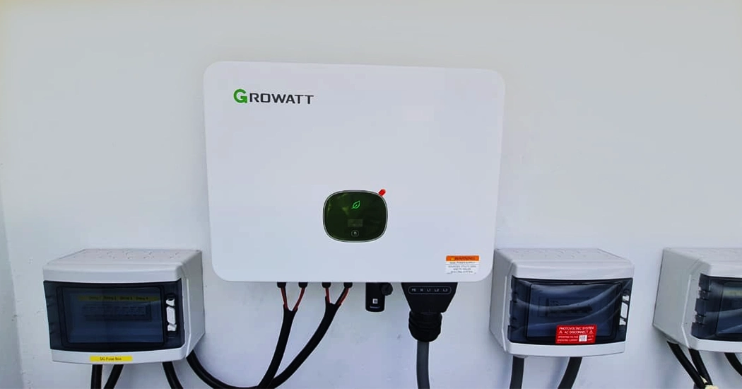 A white wall-mounted Growatt solar inverter with connected wiring and adjacent breaker boxes.