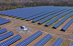 Aerial view of a ground-mounted solar panel farm integrated with a central battery energy storage unit.