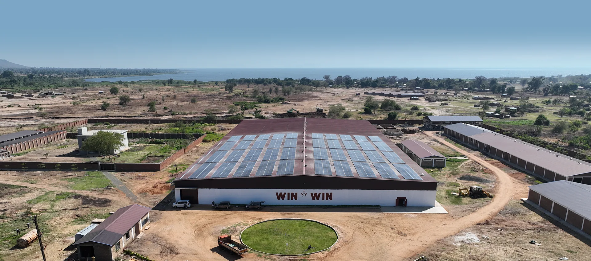 Aerial view of a commercial facility in Malawi with rooftop solar panel arrays overlooking surrounding landscapes and a nearby lake.
