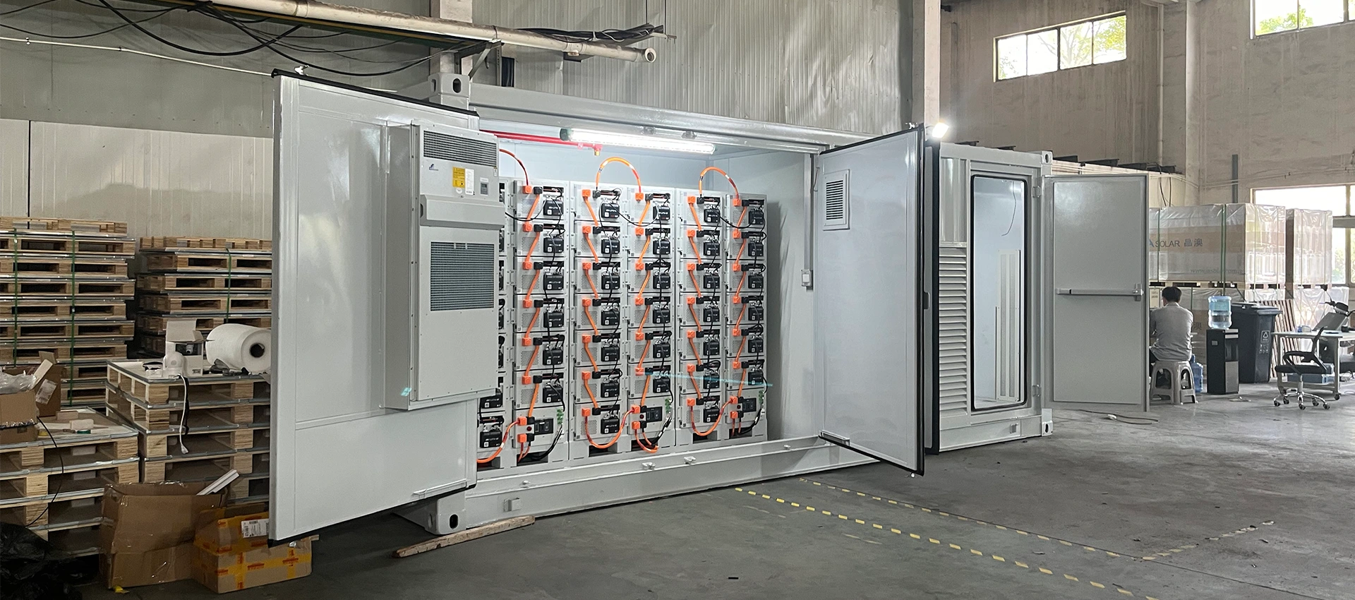 Large containerized battery energy storage system with open doors showing neatly stacked battery modules inside a warehouse.