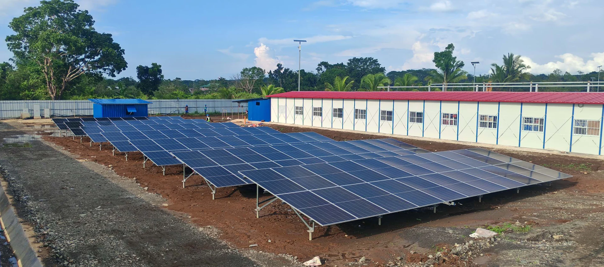 Ground-mounted solar panel array installed beside a long site office building under a blue sky in the Philippines.