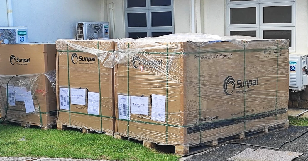 Pallets of shrink-wrapped Sunpal solar photovoltaic module crates placed outside a building.