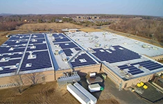 Aerial view of a large commercial facility with extensive rooftop solar panel installations integrated with energy storage infrastructure.