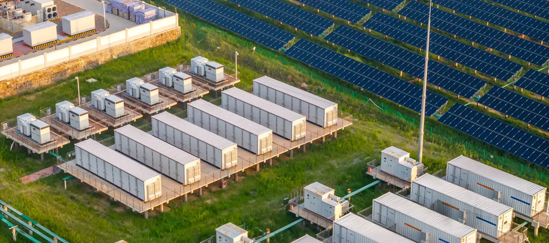 Aerial view of a large containerized battery energy storage installation situated alongside a solar PV panel farm.