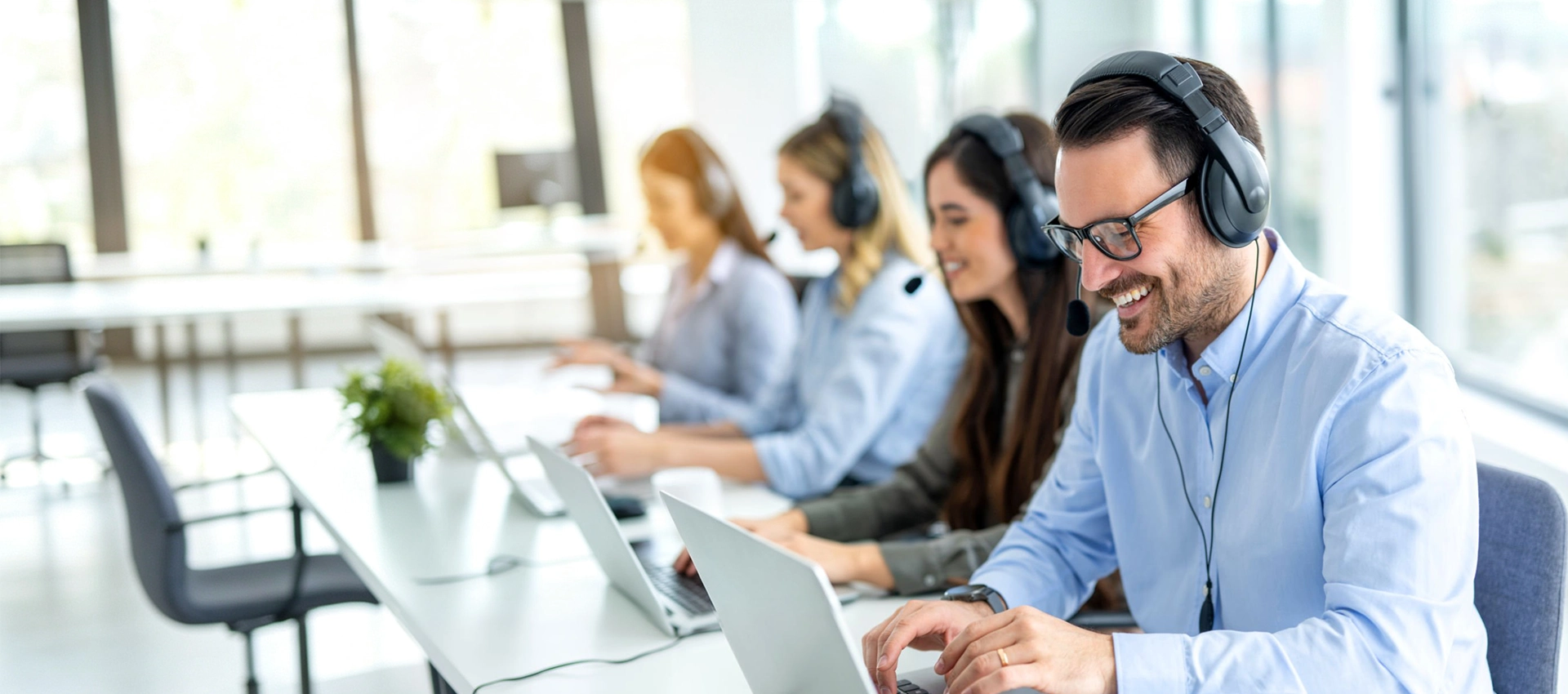 Smiling Sunpal customer service representatives wearing headsets and working on laptops in a modern office, ready to answer frequently asked questions.