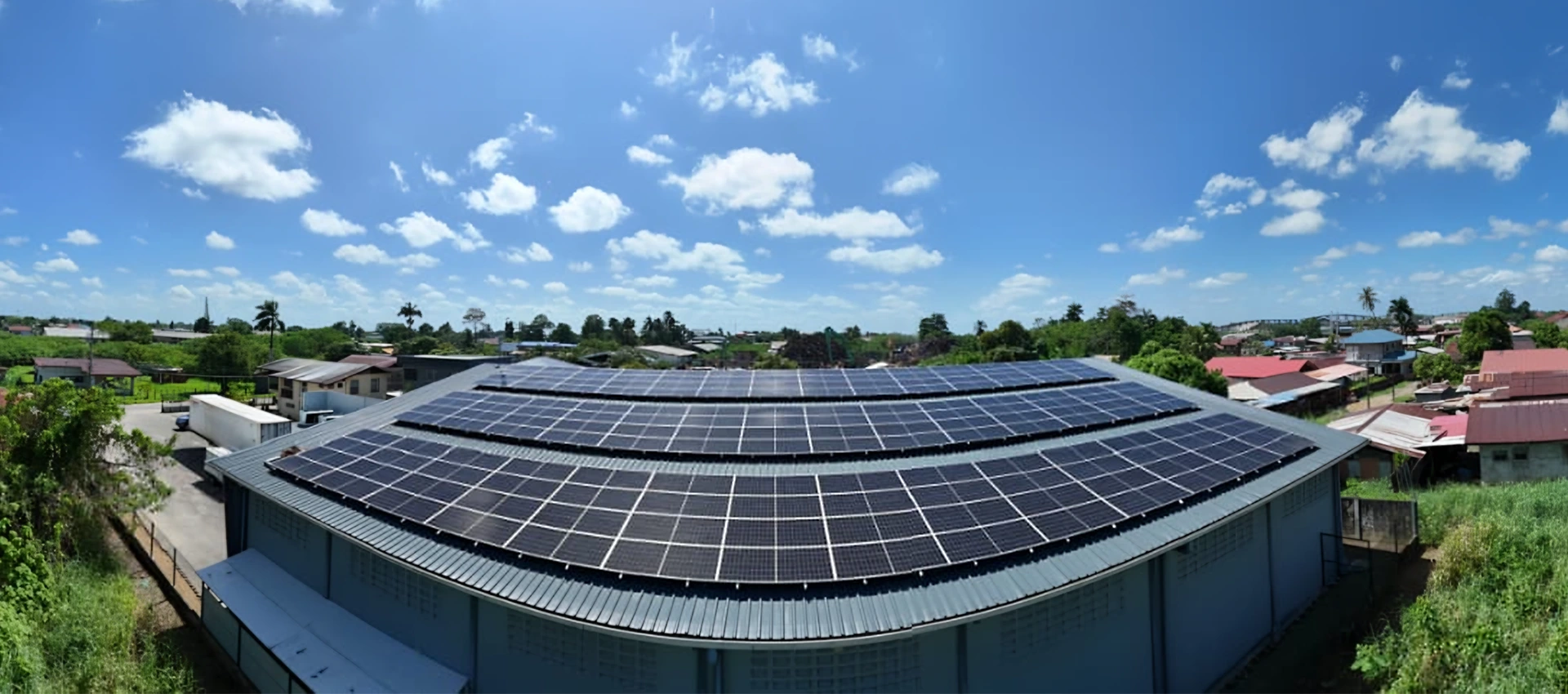 Wide aerial shot of a rooftop solar array installed on a large facility under a clear blue sky in Suriname.