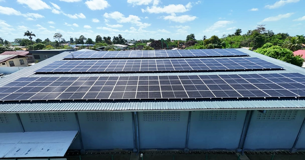 Elevated view of multiple rows of solar panels mounted on the pitched metal roof of a commercial facility in Suriname.