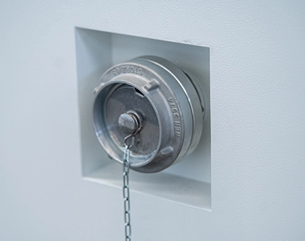 Stainless steel Storz fire water connection inlet with protective cap mounted on the side wall of a BESS enclosure.